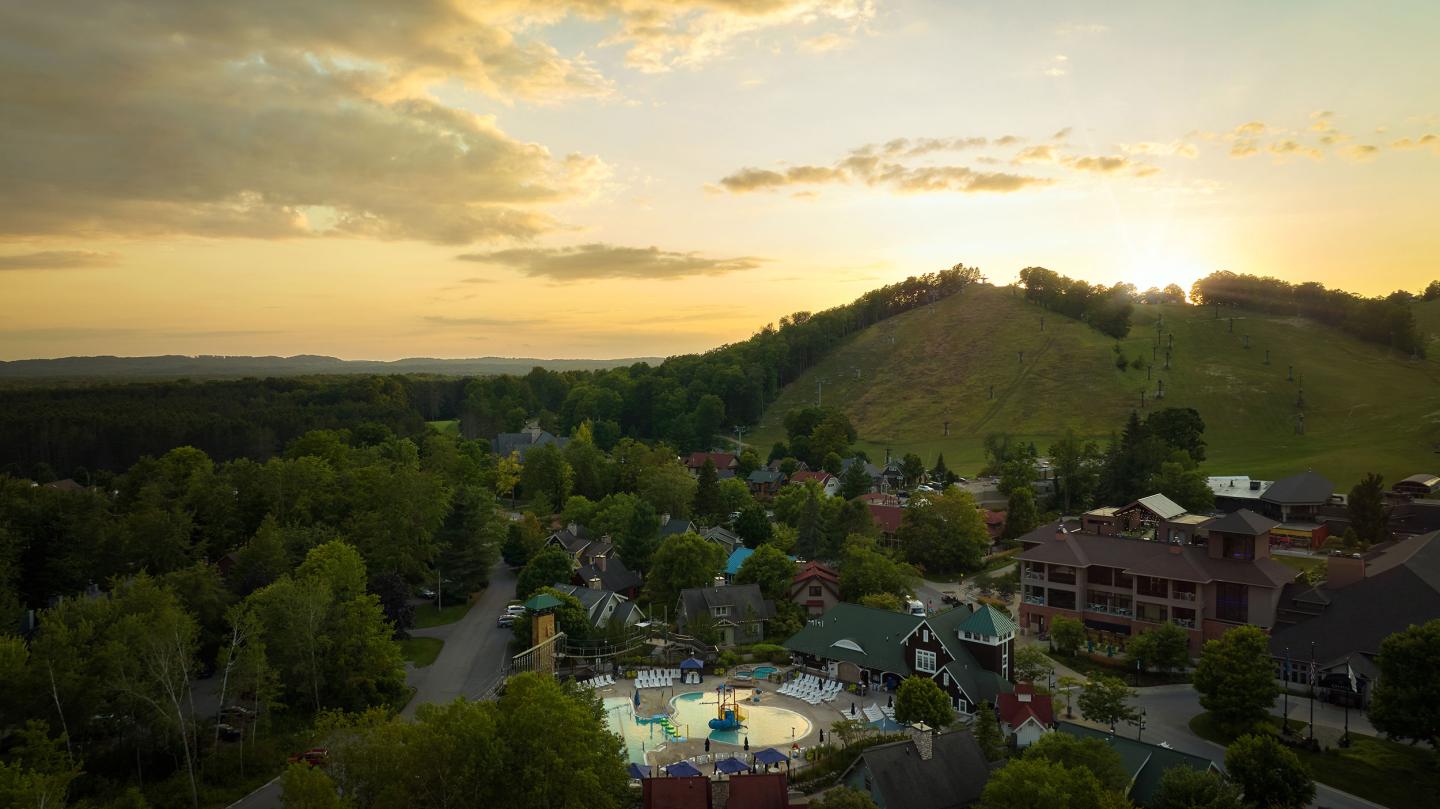 Aerial view of a resort near a hill at sunset, surrounded by trees and buildings.