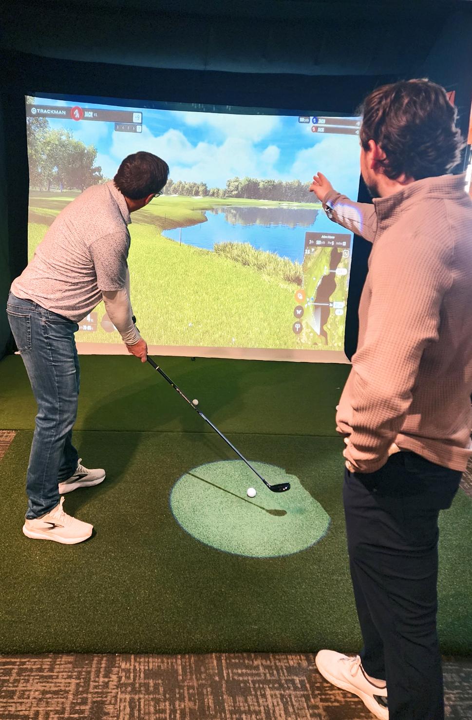 Two people playing virtual golf indoors, focused on a screen showing a golf course.