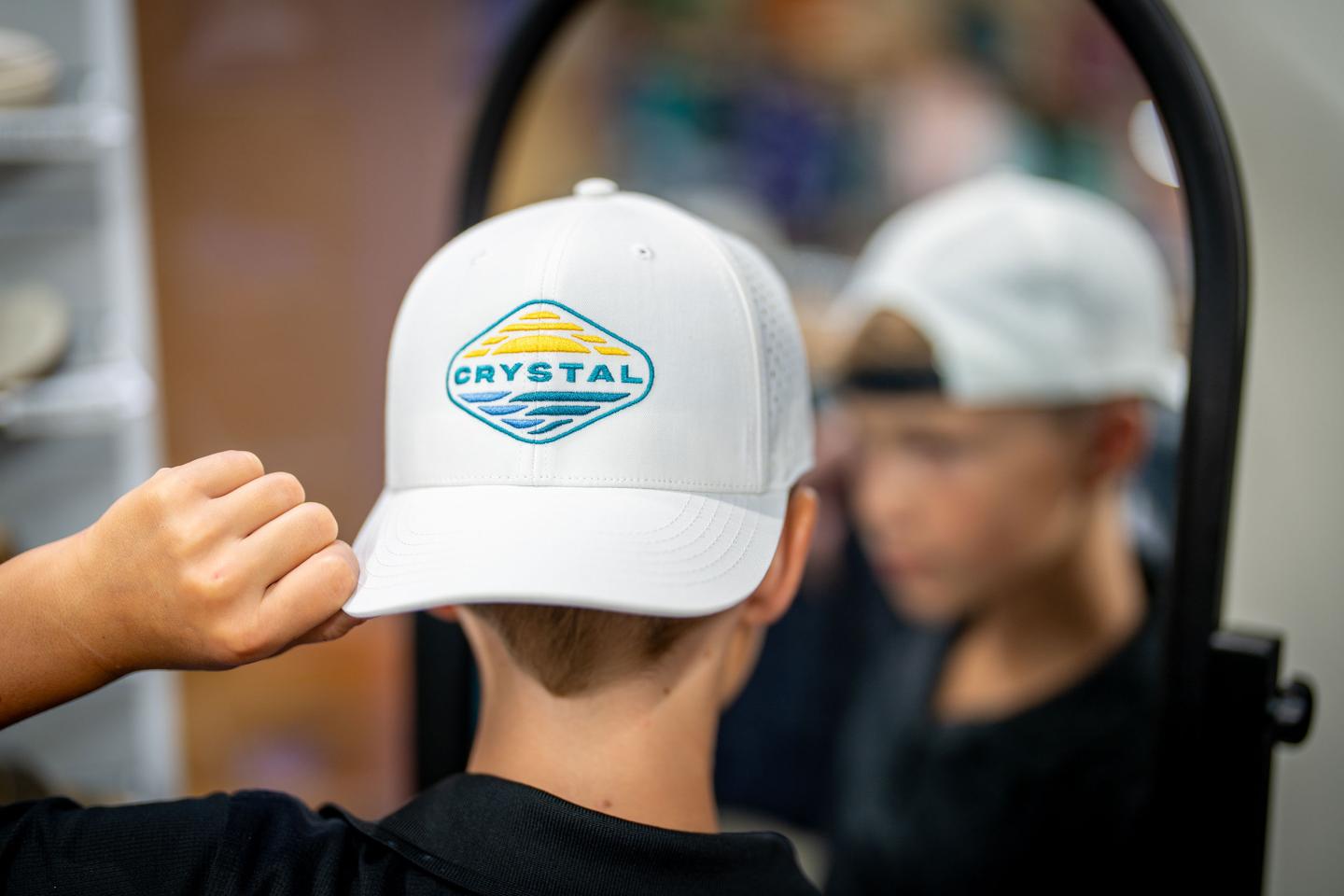 Young boy wearing a white cap with a logo, looking into a mirror.