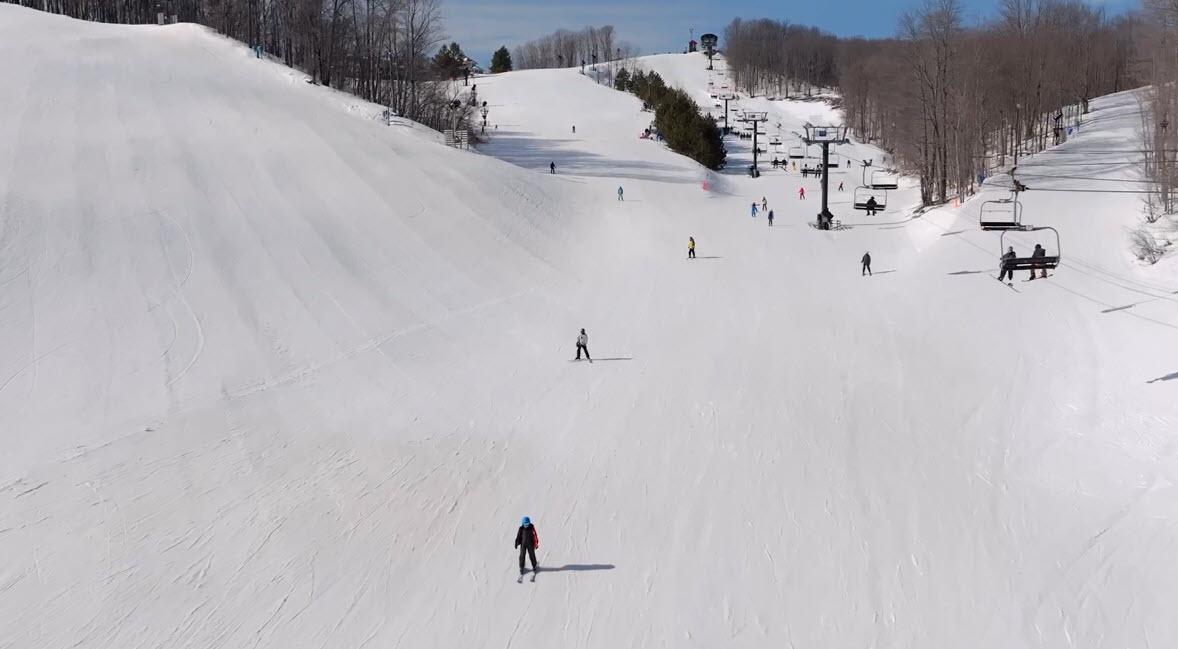 Snowy ski slope with skiers descending under a clear blue sky.
