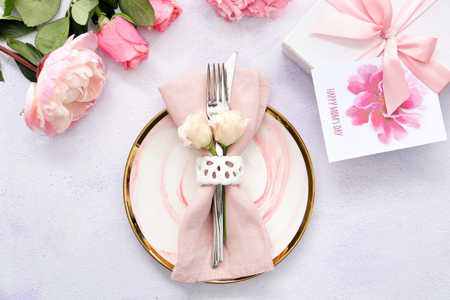 Pink table setting with roses, napkin, fork, and knife on a patterned plate.