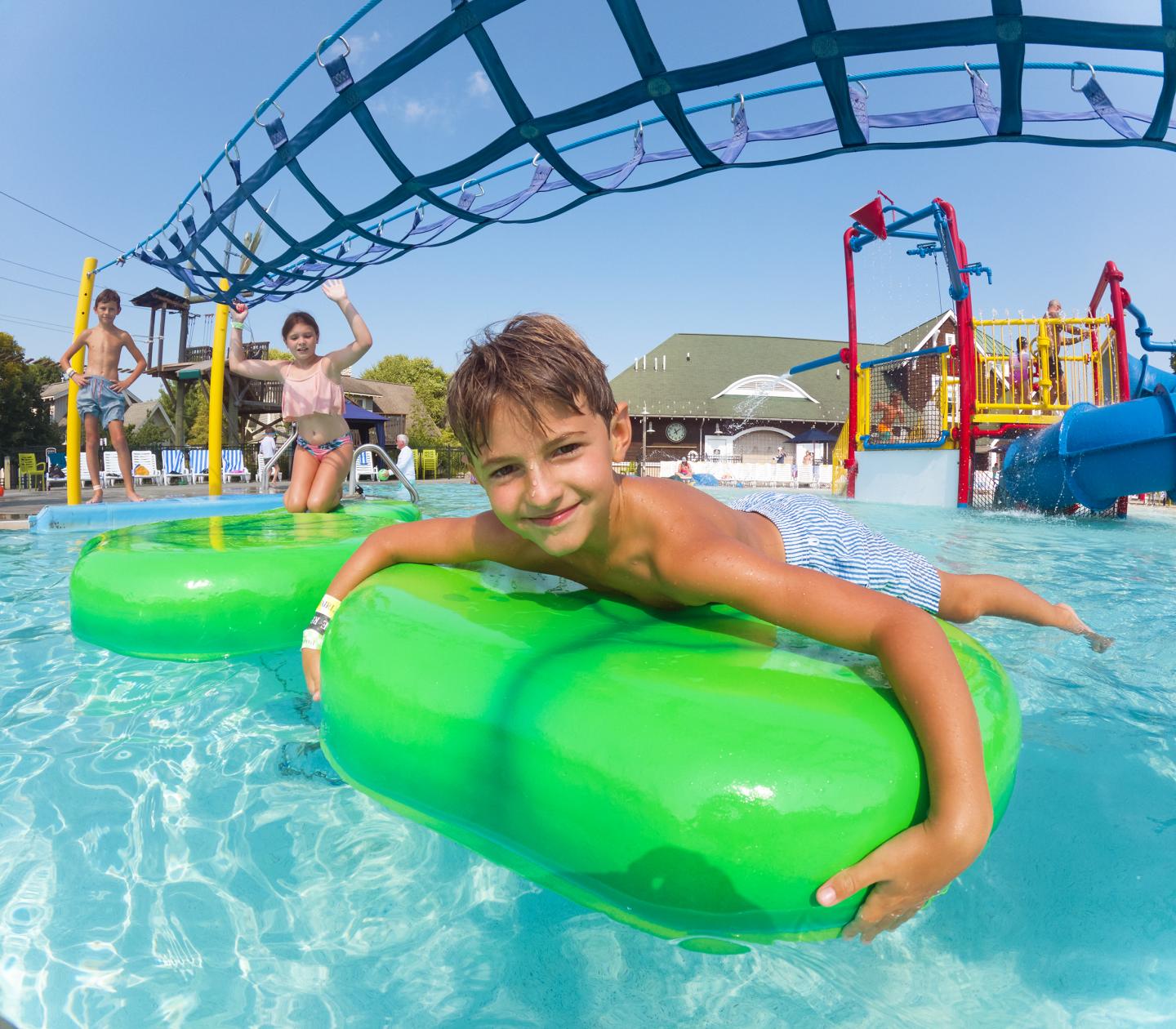 Boy smiling on a green float in a colorful water park.