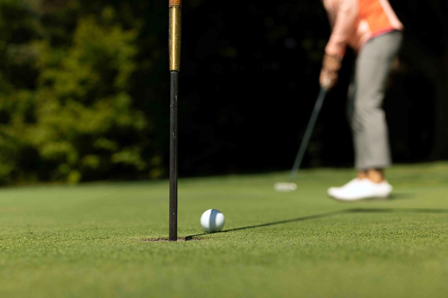 Golf player putting on green, ball near hole.