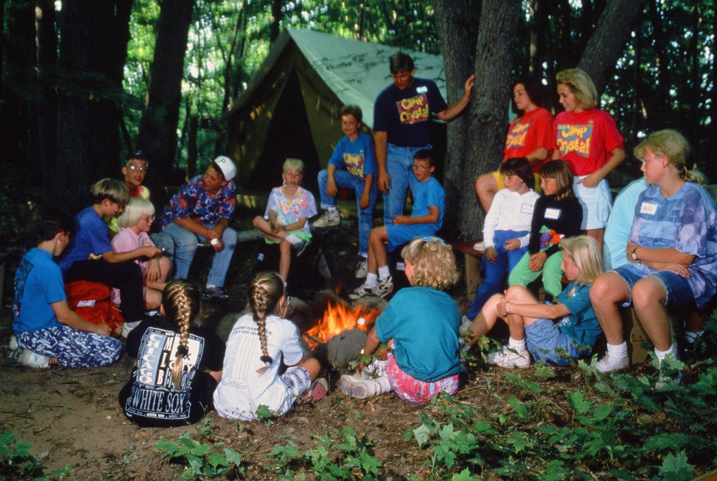Campers gathered around a campfire in a forest setting.