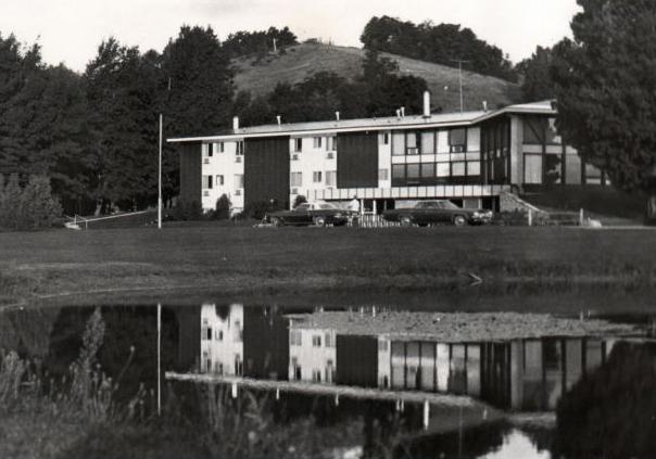 Modern building by a pond, trees in the background, black and white photo.
