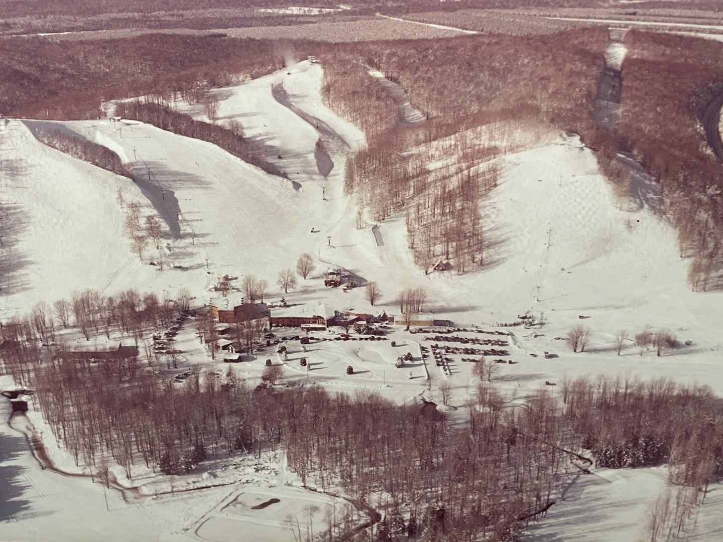 Aerial view of snowy ski slopes and wooded area.