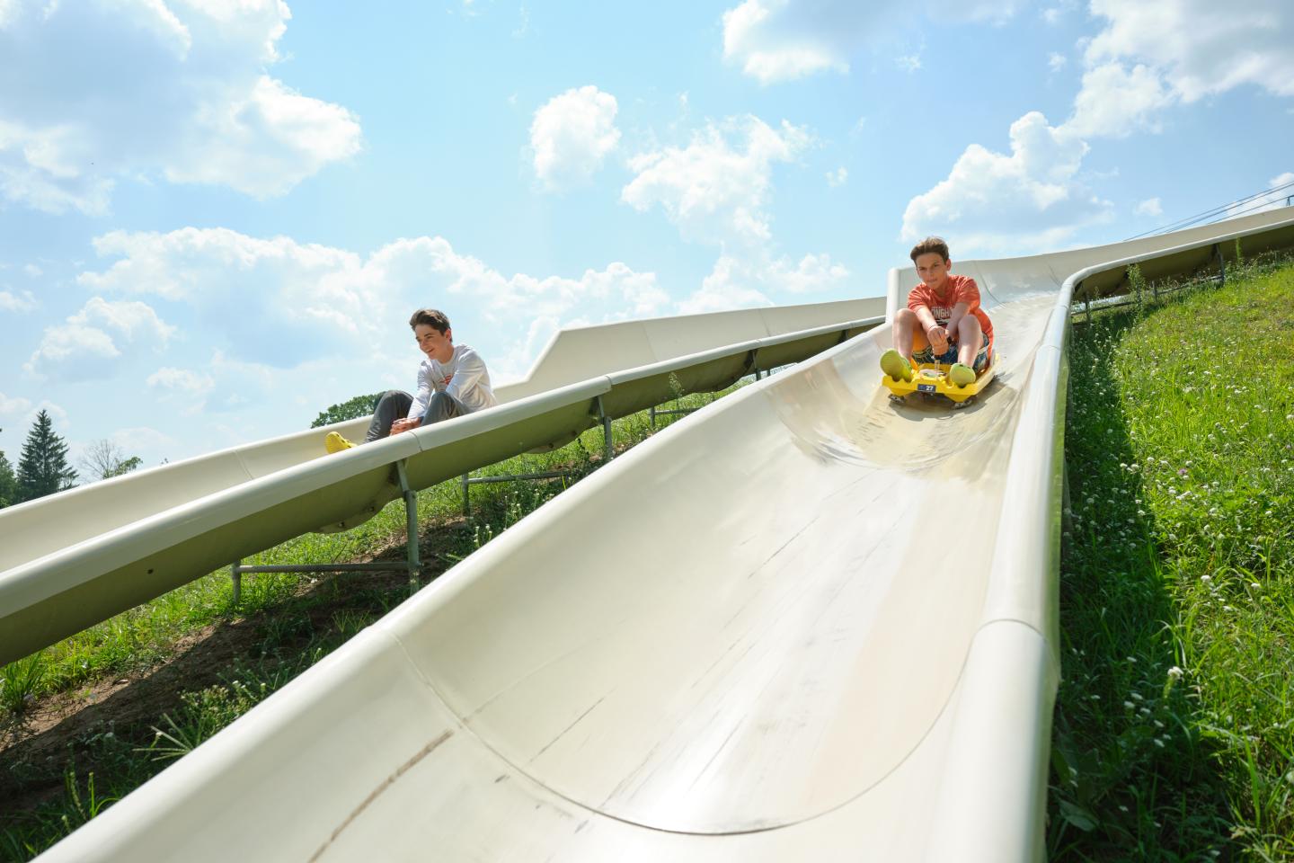 Two people sliding down parallel slides on a sunny day.