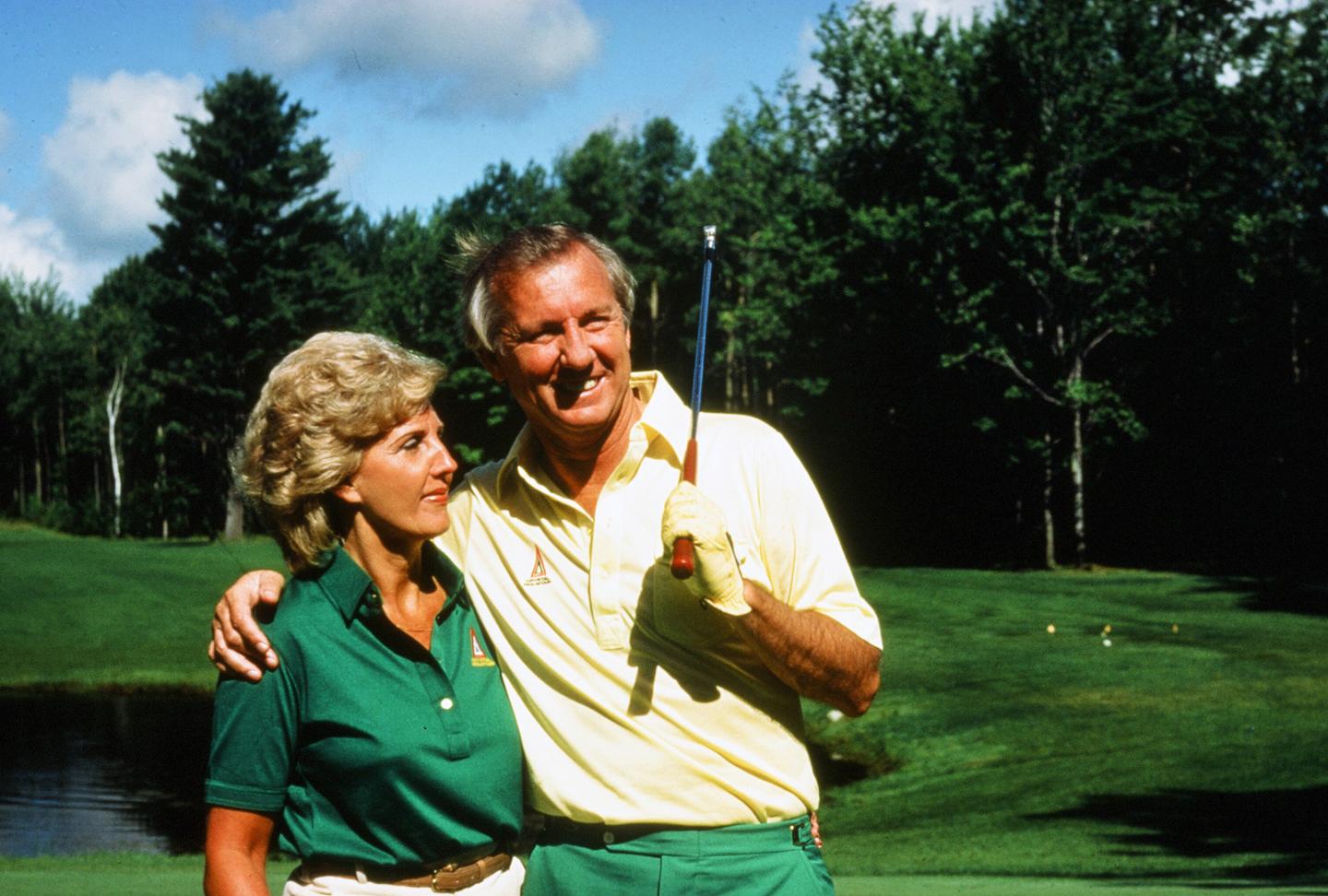 Smiling couple on a golf course with trees in the background.