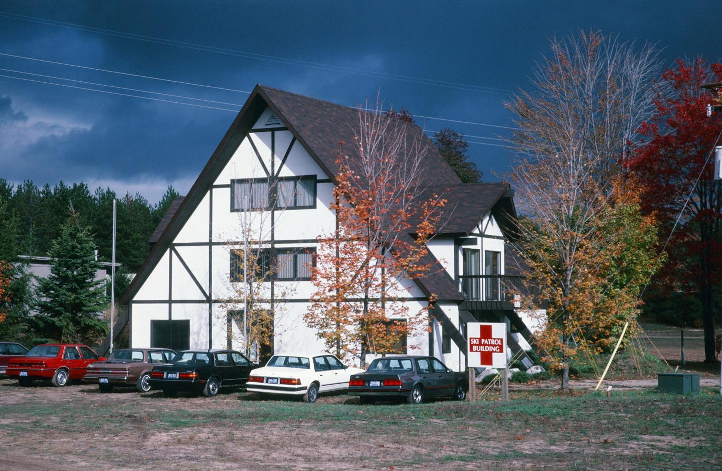 A-frame house with fall foliage and parked cars under a cloudy sky.