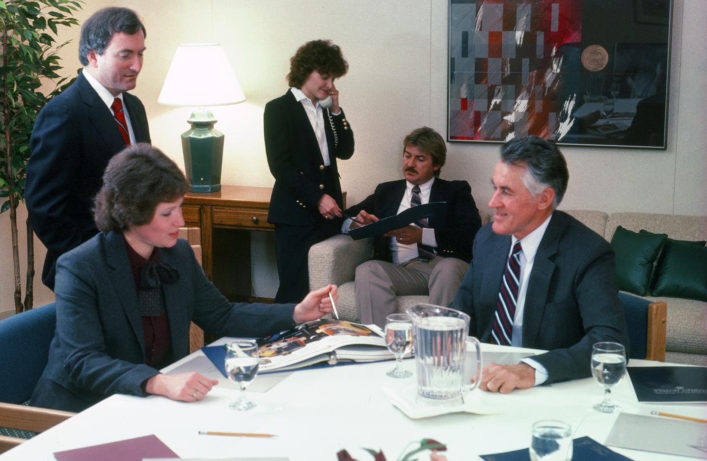 Colleagues in a meeting room, discussing documents at a table.