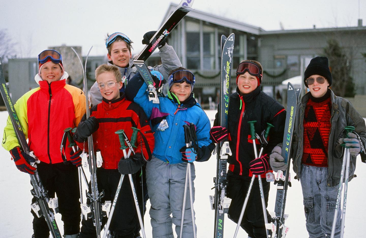 Group of skiers holding poles, dressed in colorful winter gear, snowy backdrop.