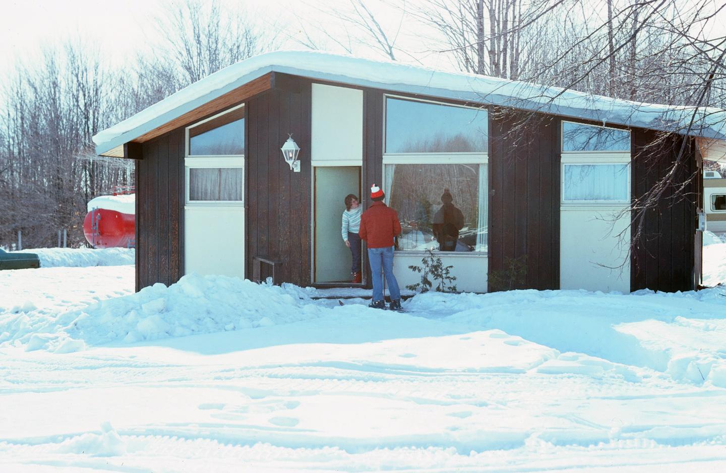 Modern cabin in snowy landscape, two people by the door.