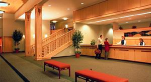 Hotel lobby with wooden decor, front desk, and staircase. Guests interacting with staff.
