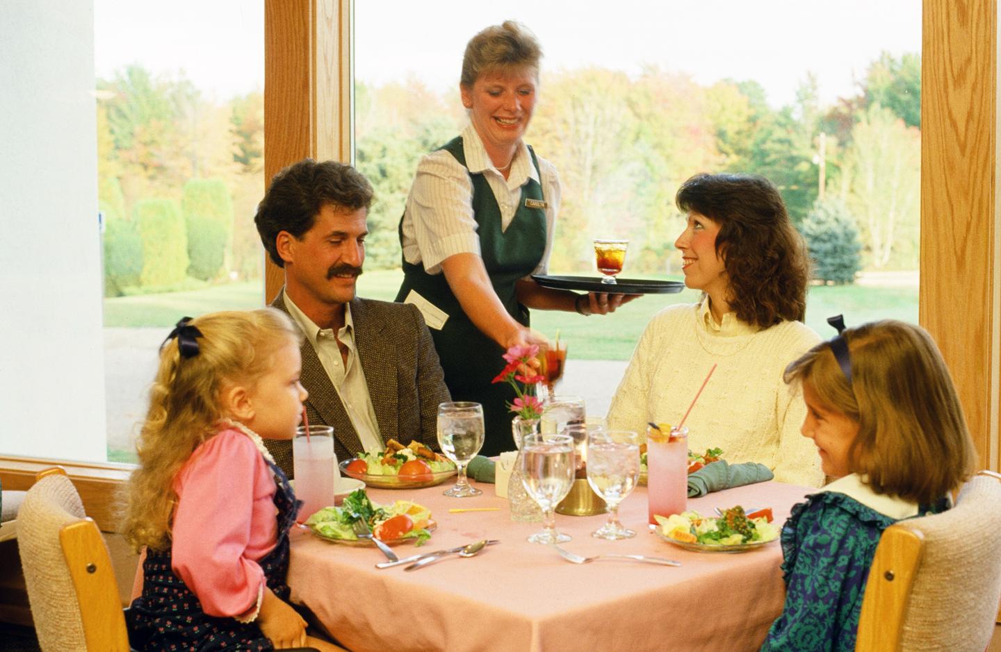 Family dining at a restaurant with a waitress serving drinks.