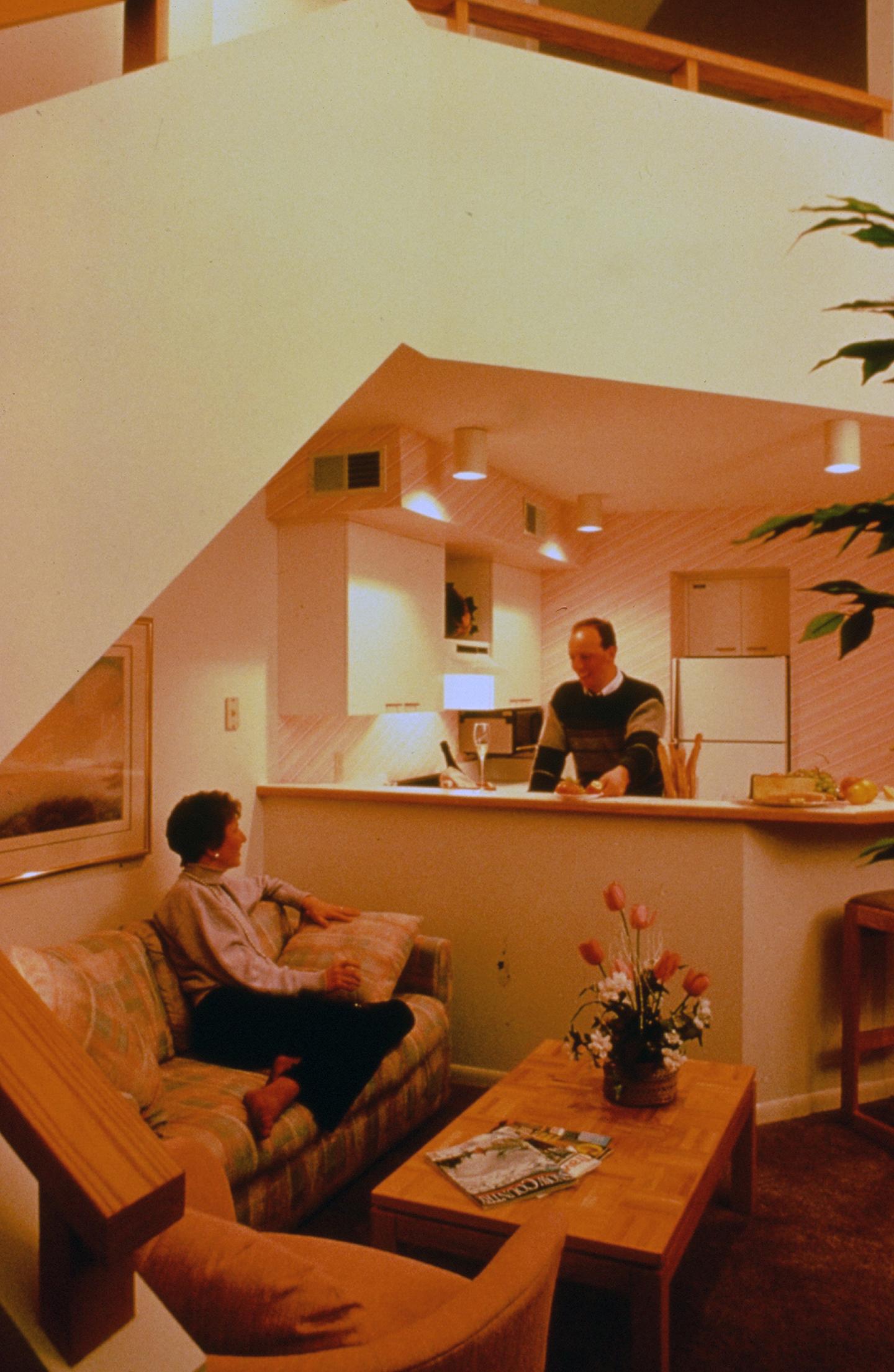 Man and woman in a warmly lit living room and kitchen.