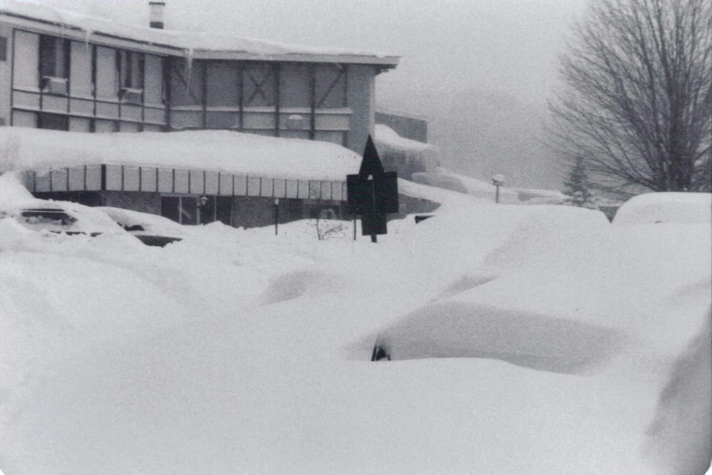 Snow-covered street and cars next to a building in winter.