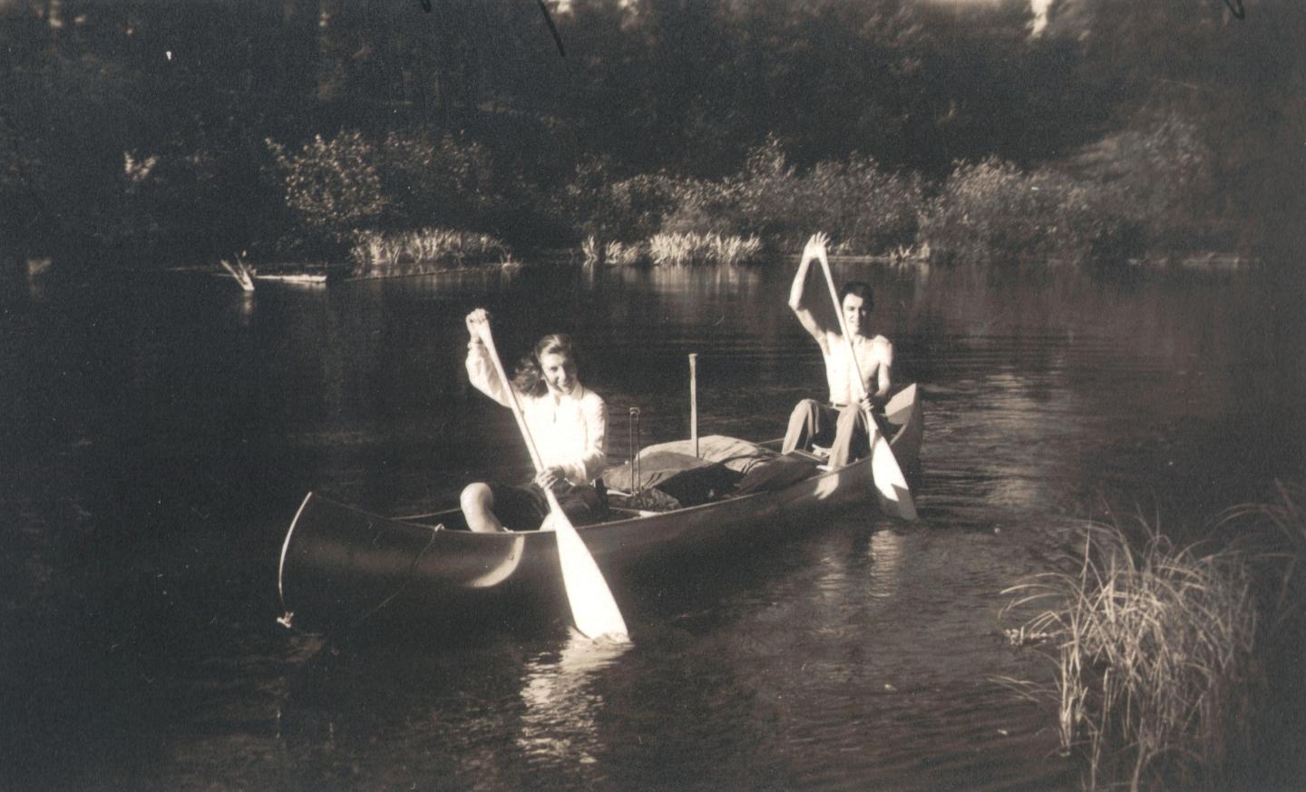 Two people paddling a canoe on a calm river.