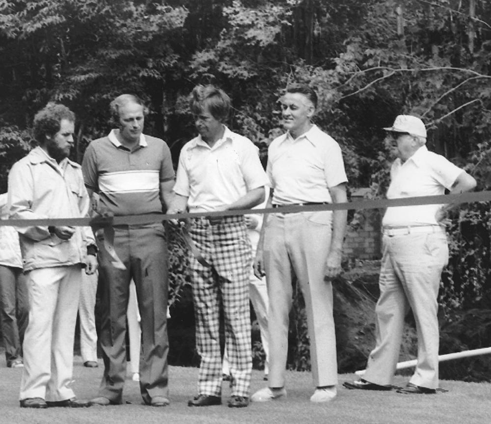 Five men standing near a ribbon in a forest setting.