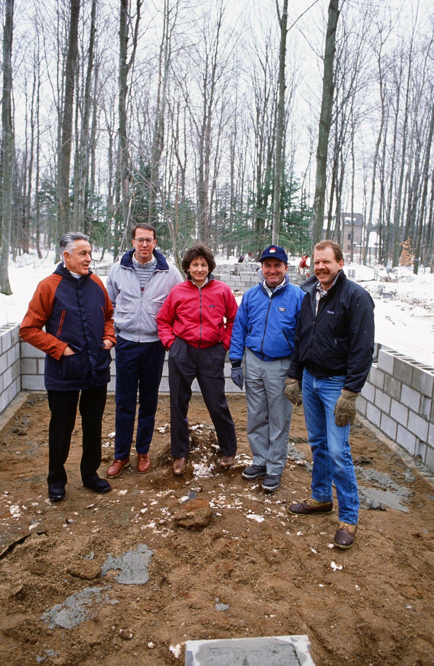 Five people standing on a sandy area, surrounded by snow and trees.