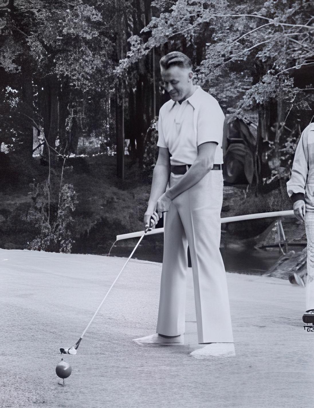 Golfer swinging club outdoors on grass, vintage black-and-white photograph.
