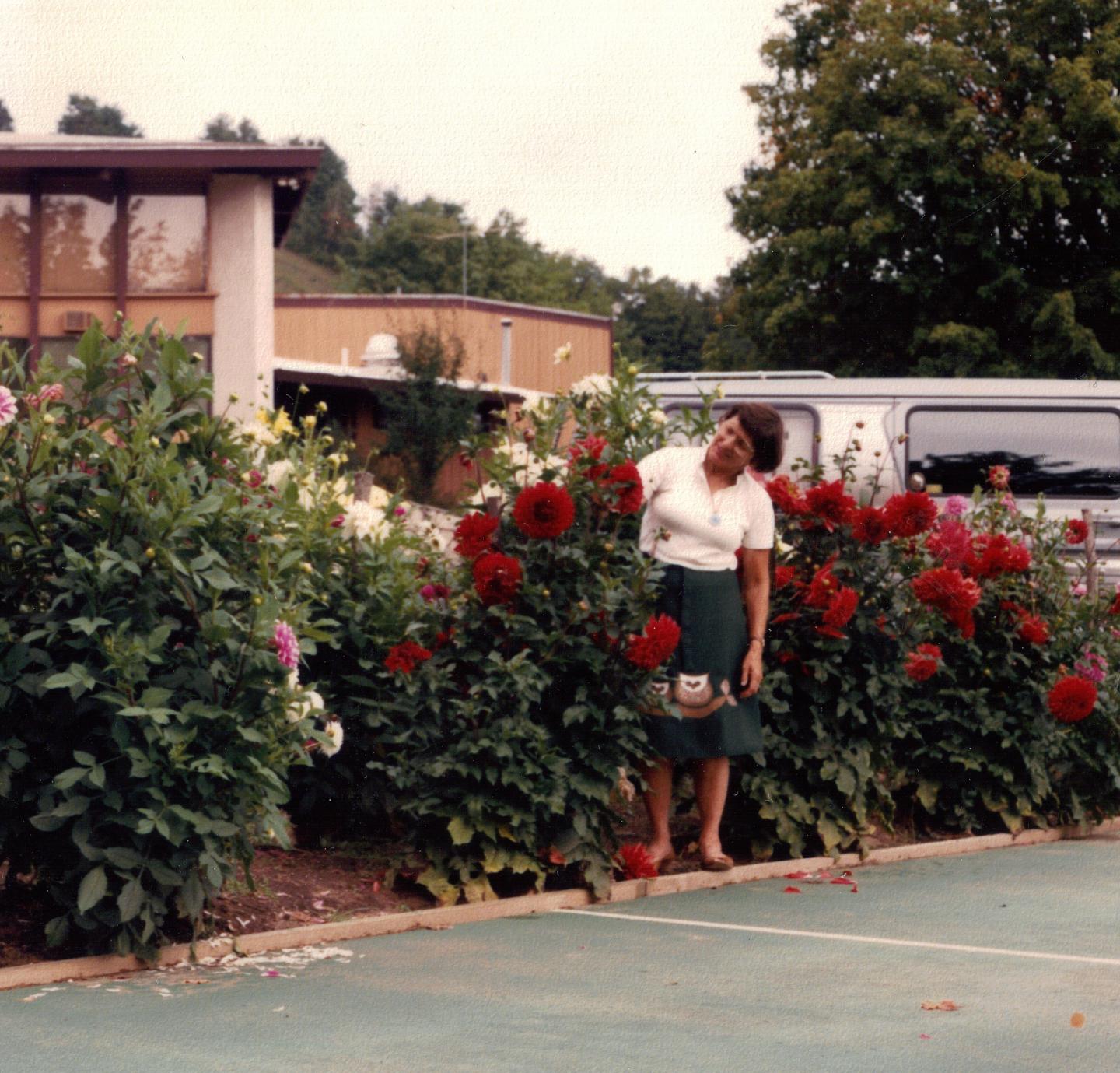 Woman smiling near red flowers by a tennis court.