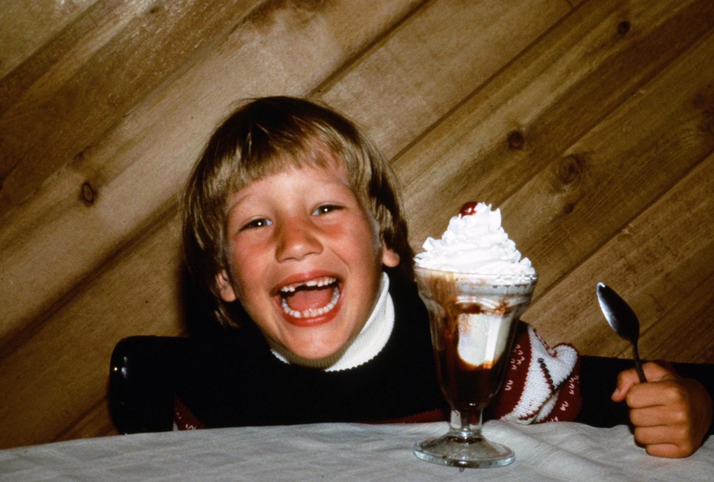 Smiling child with an ice cream sundae, wooden wall background.