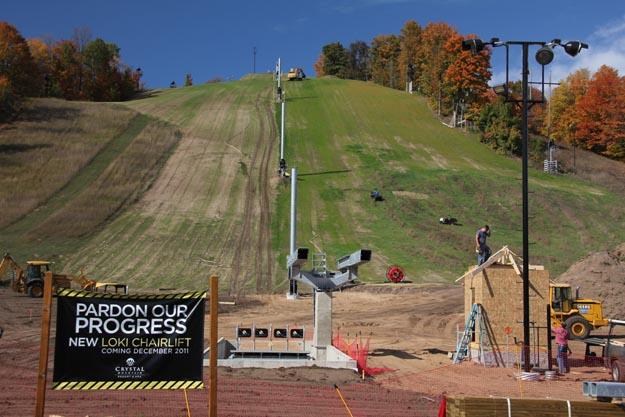 Ski resort under construction on a grassy hill with autumn trees.