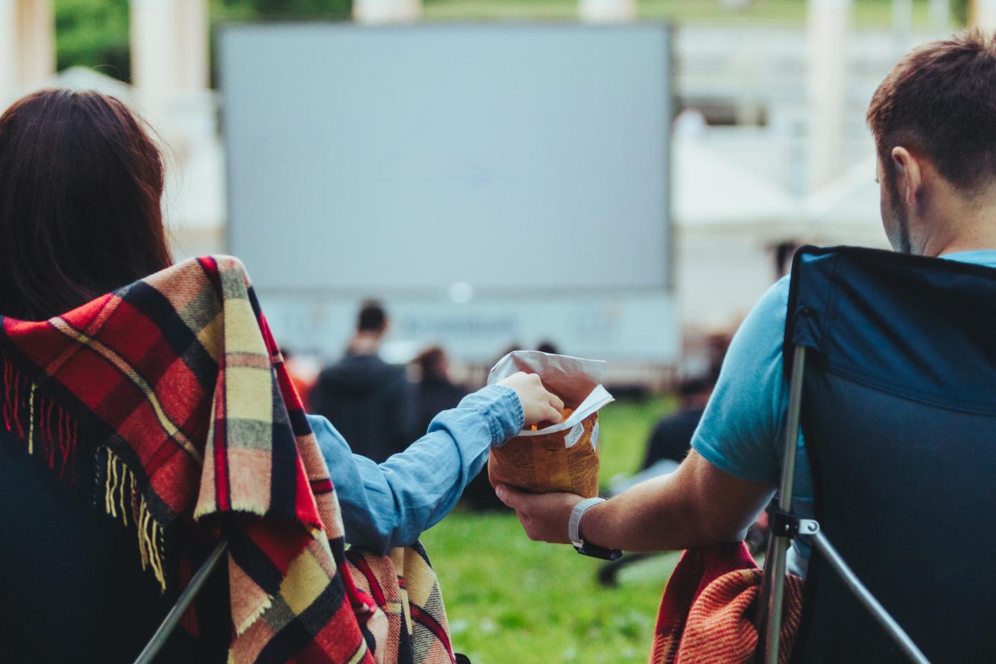 Outdoor movie night with two people sharing snacks in lawn chairs.