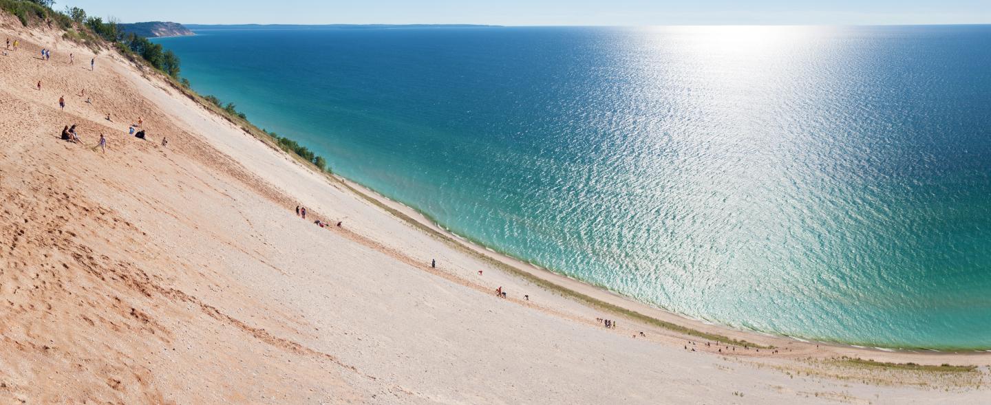 Steep sandy dune overlooking a vast, shimmering blue lake.
