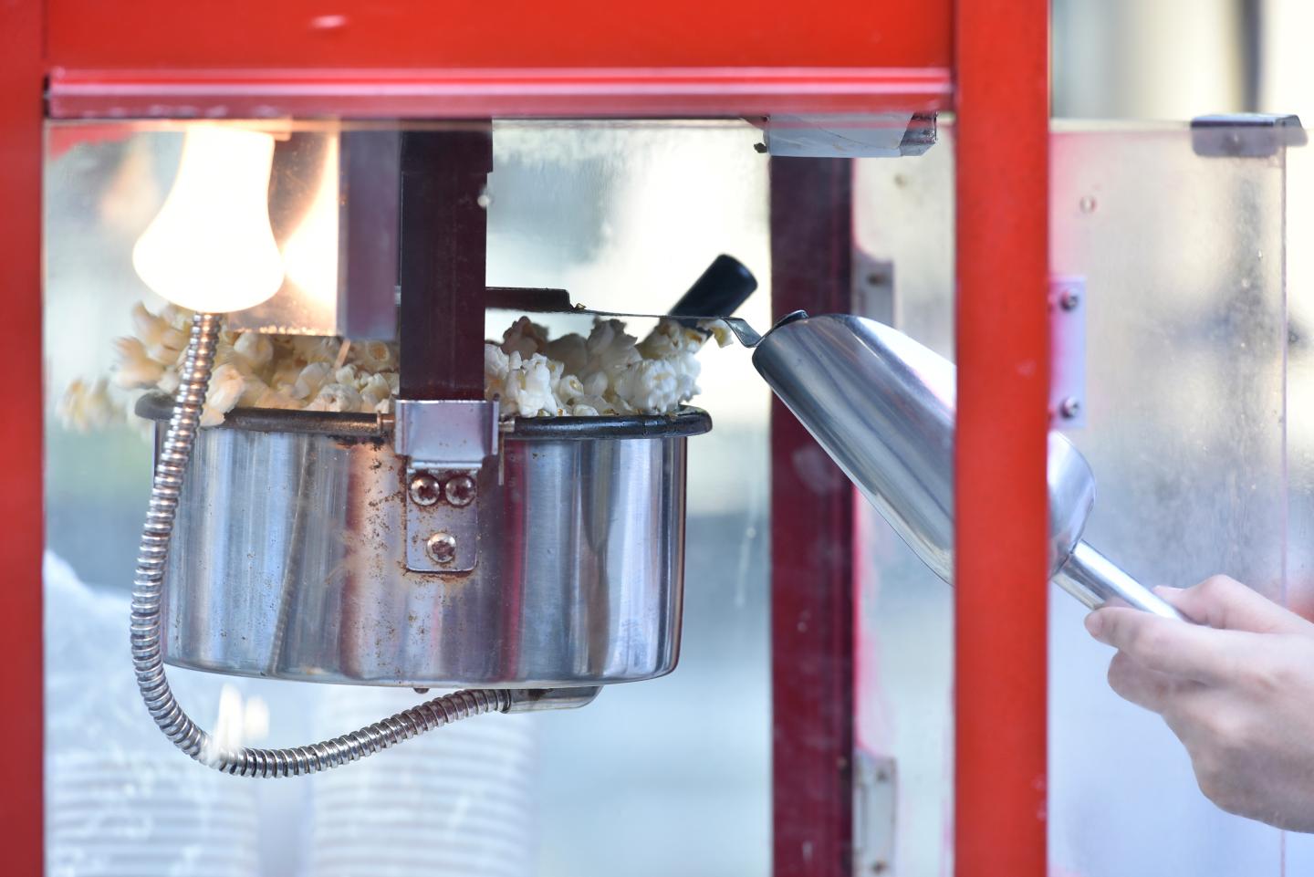 Popcorn popping in a red machine with a scooper nearby.