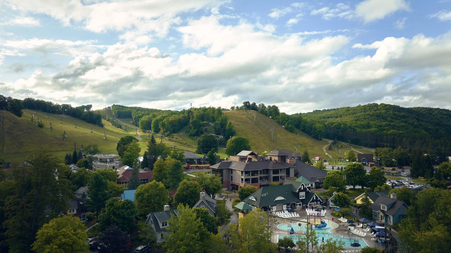 Scenic village and ski hills under cloudy sky.