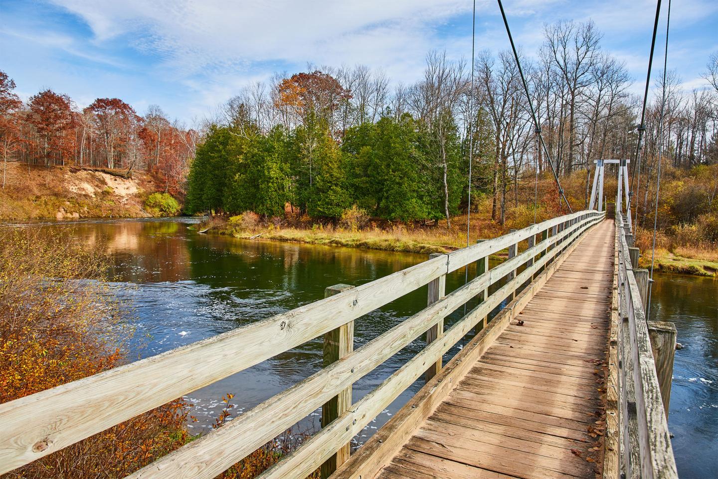 Wooden bridge over a river surrounded by autumn trees.
