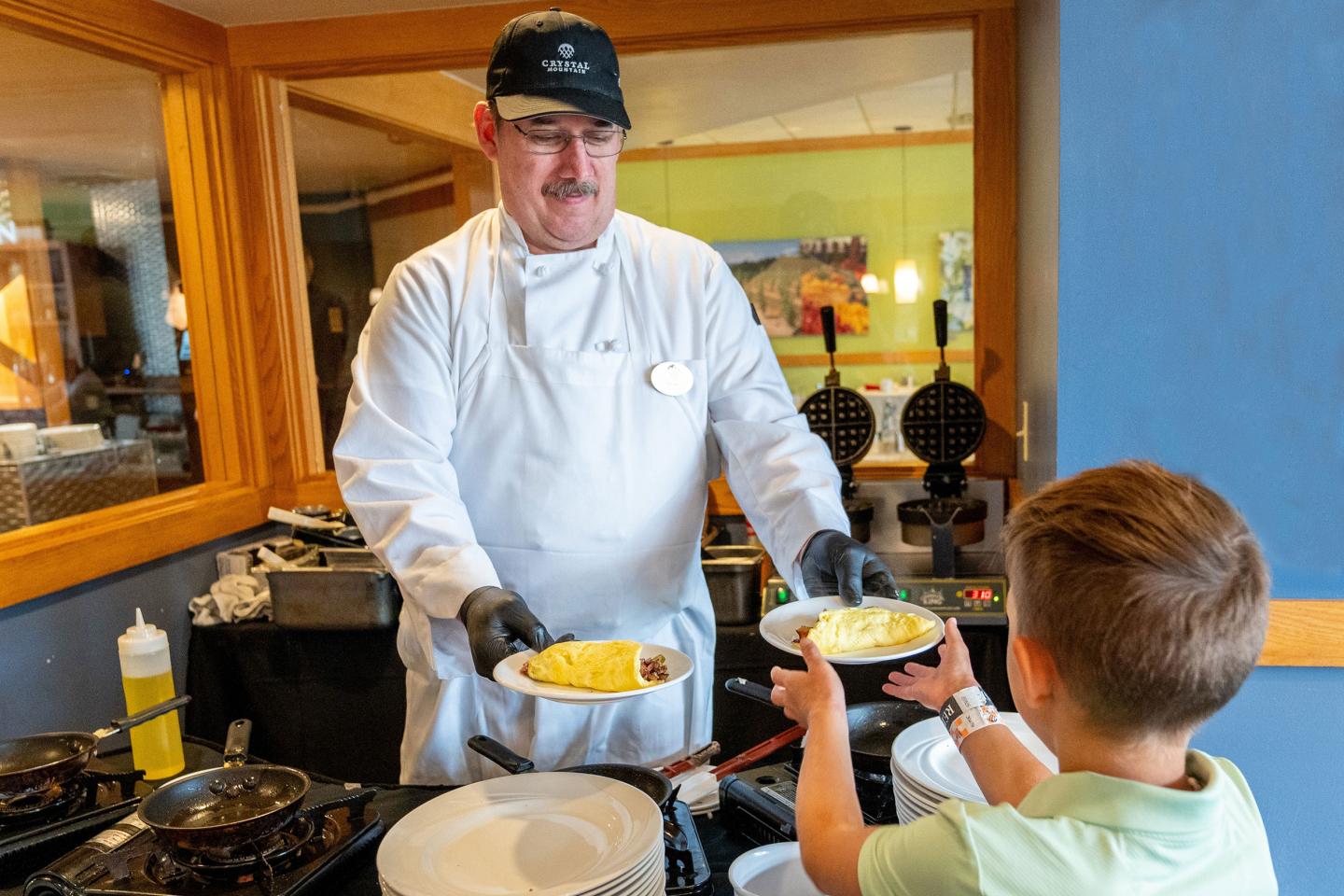 Chef serving breakfast to a child at a buffet.