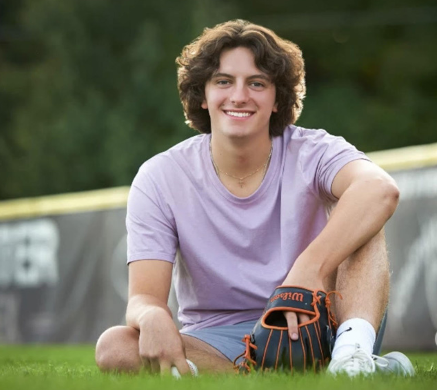 Smiling person sitting on grass with a baseball glove.