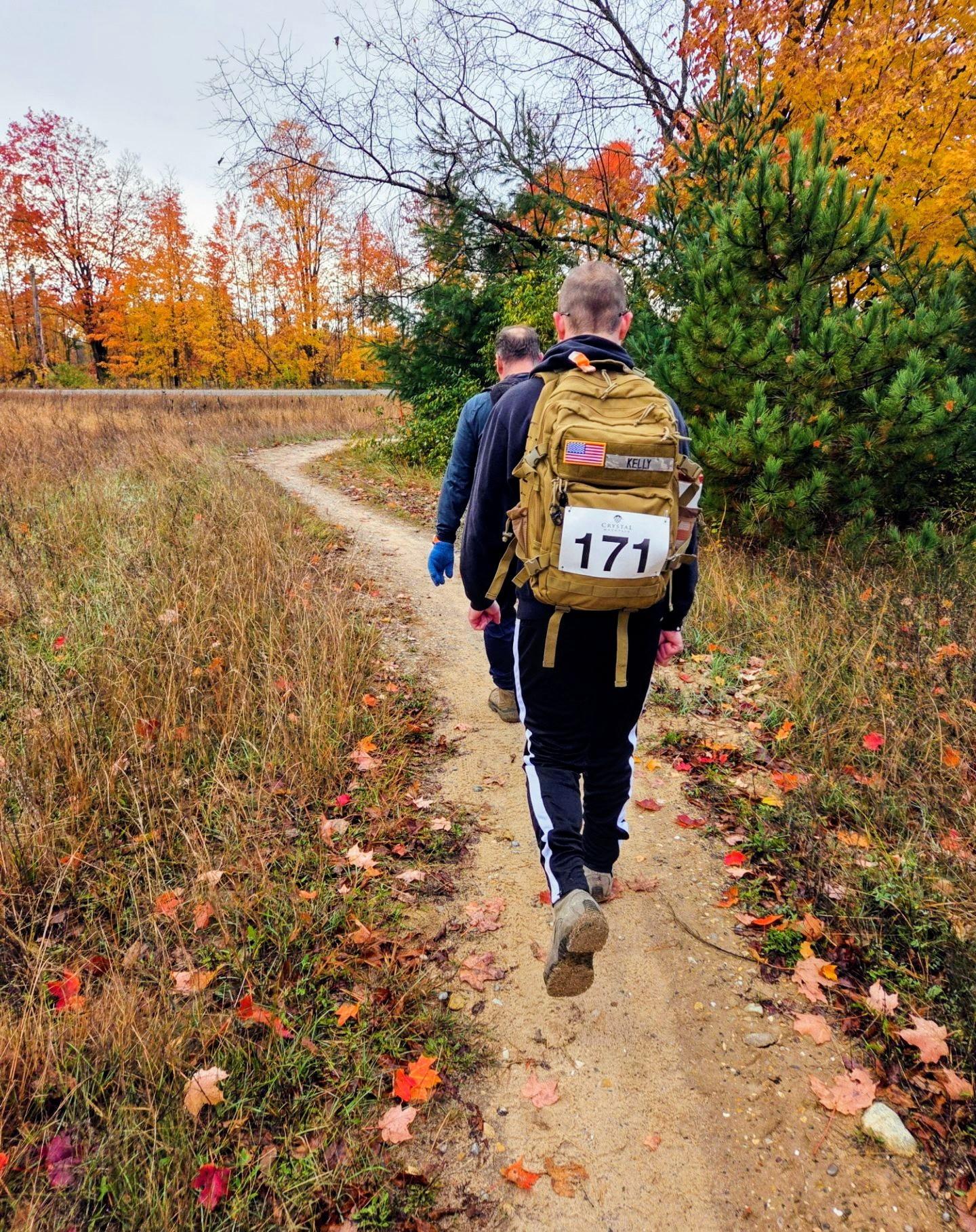 Two people hiking on a forest trail in autumn, one with a backpack numbered 171.