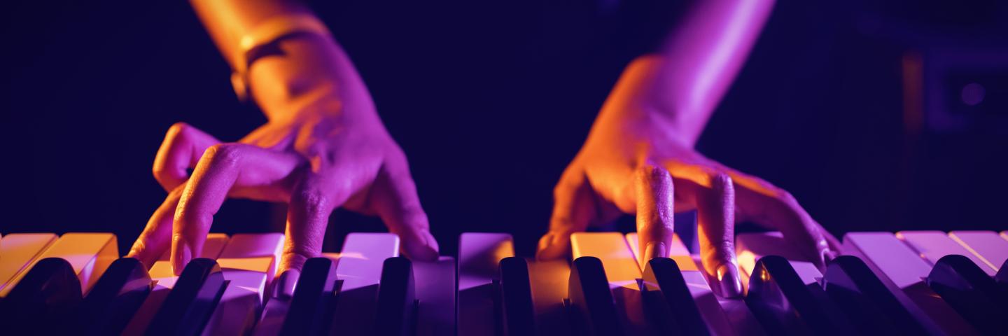 Hands playing piano under purple lighting.