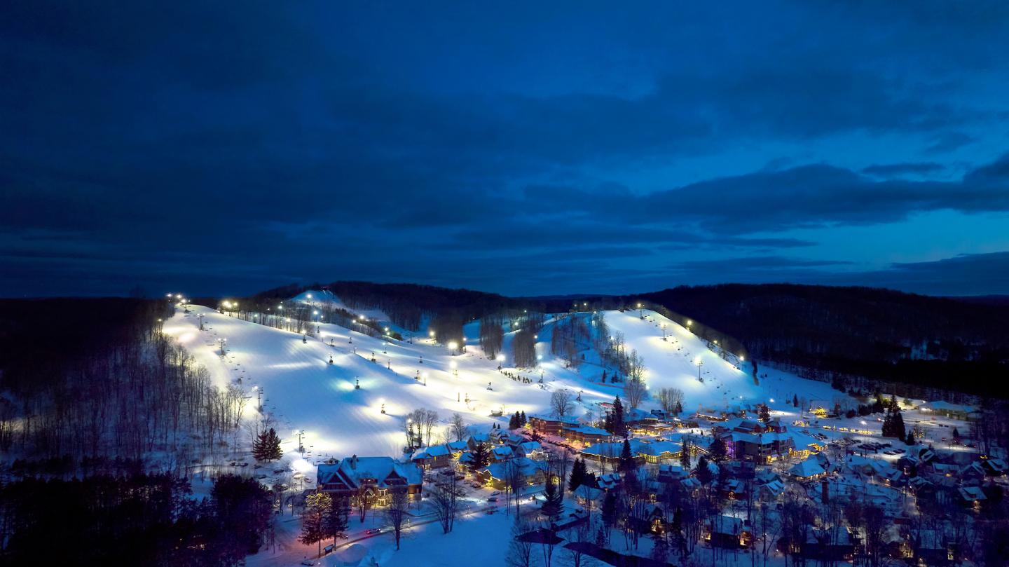 Snowy ski resort lit up at night under a deep blue sky.