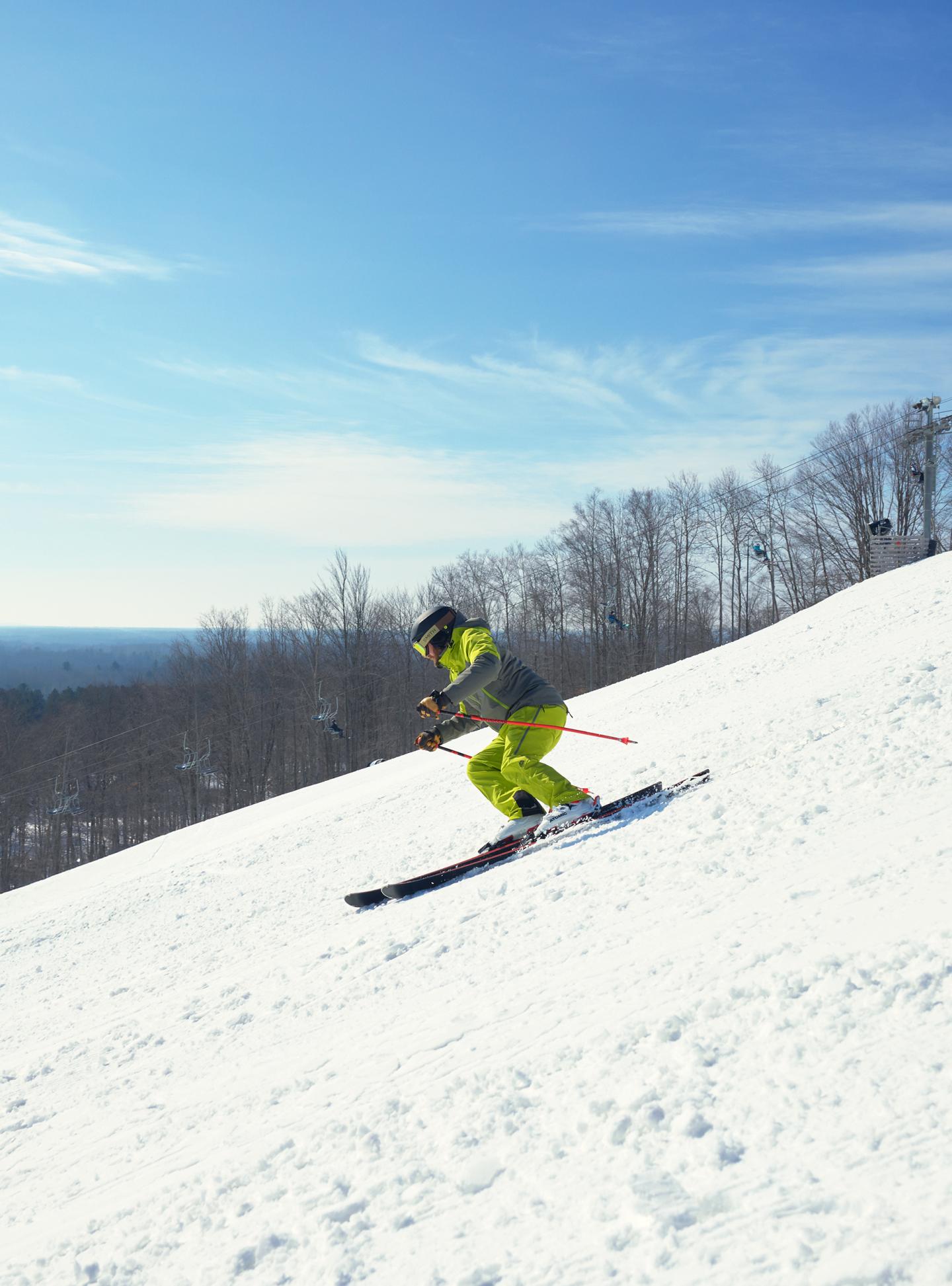 Skier in yellow gear descends snowy slope under clear blue sky.