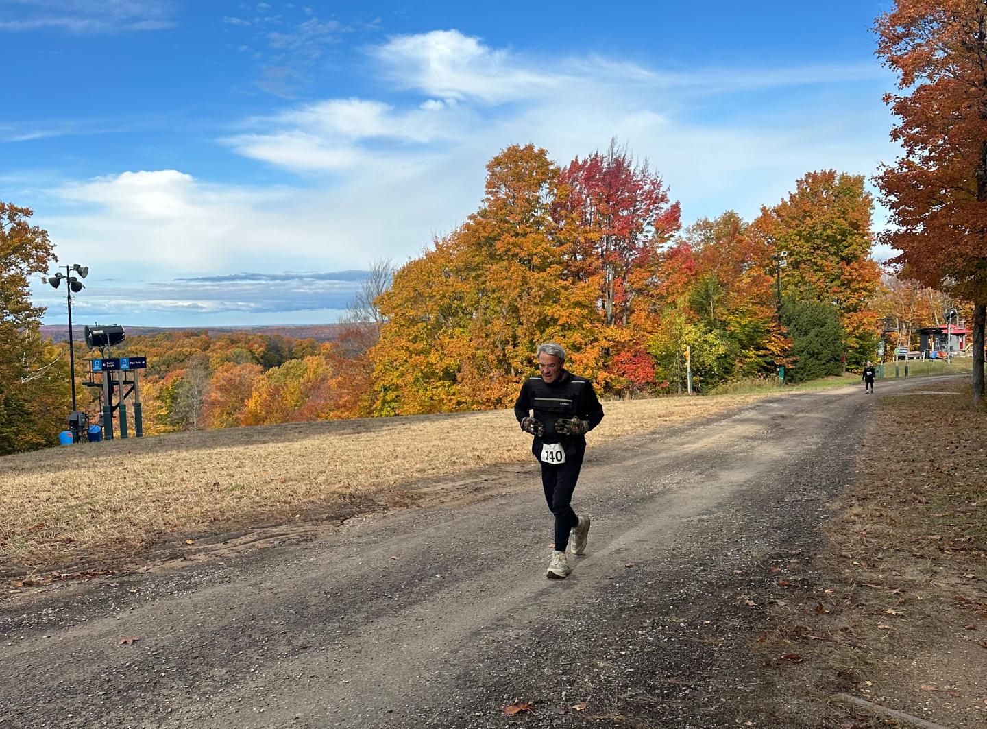 Runner on a path with autumn trees and blue sky in the background.