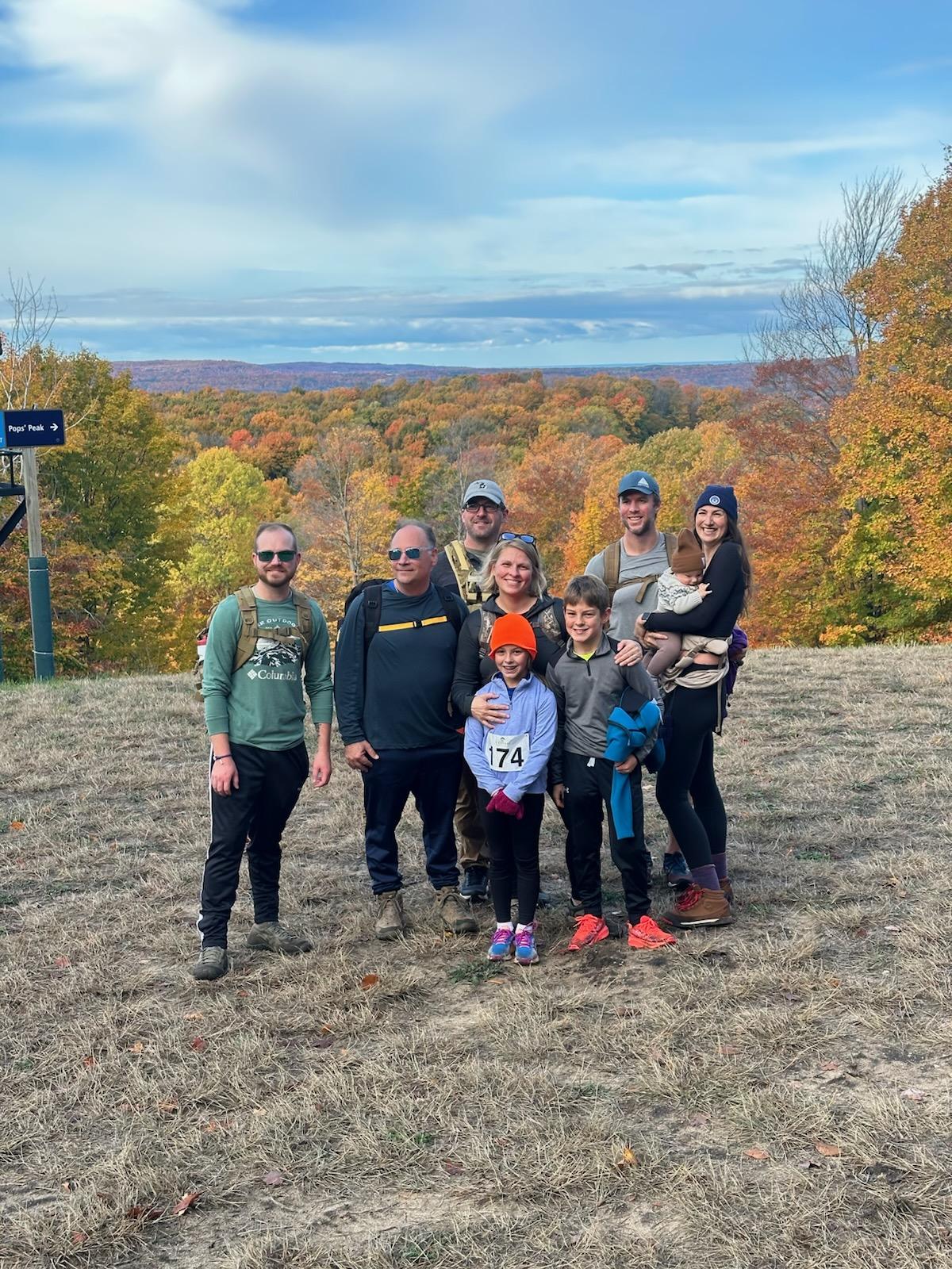 Group of people posing outdoors on grassy hill with autumn trees in the background.