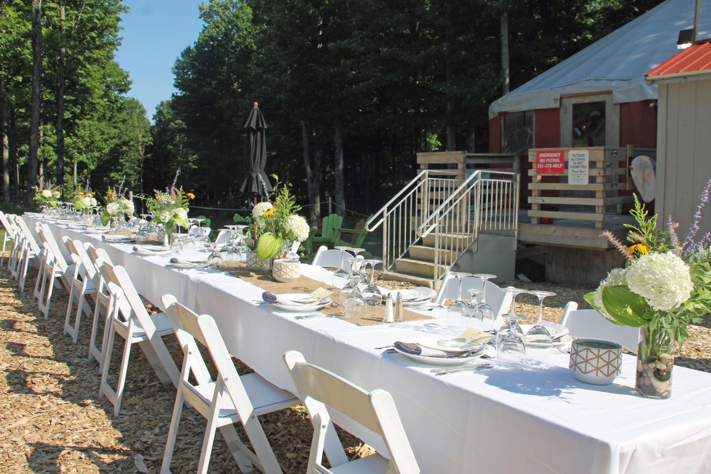 Outdoor dining setup with long tables, white chairs, and floral centerpieces.