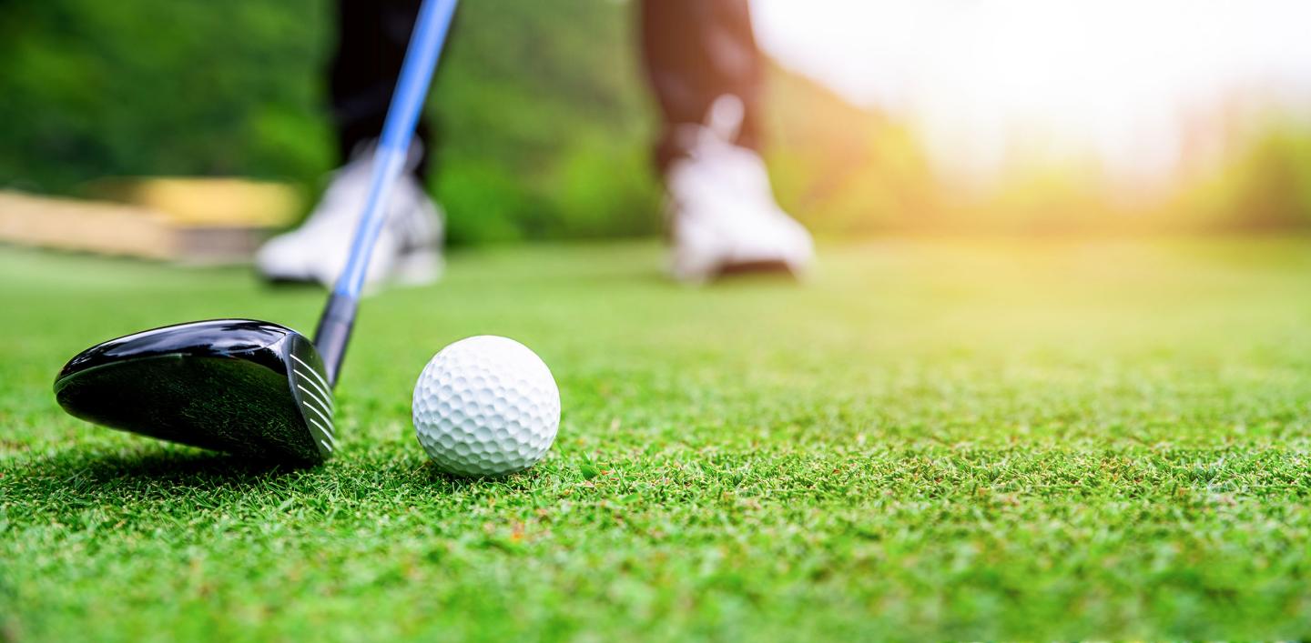 Golfer prepares to hit a ball on a sunny green course.