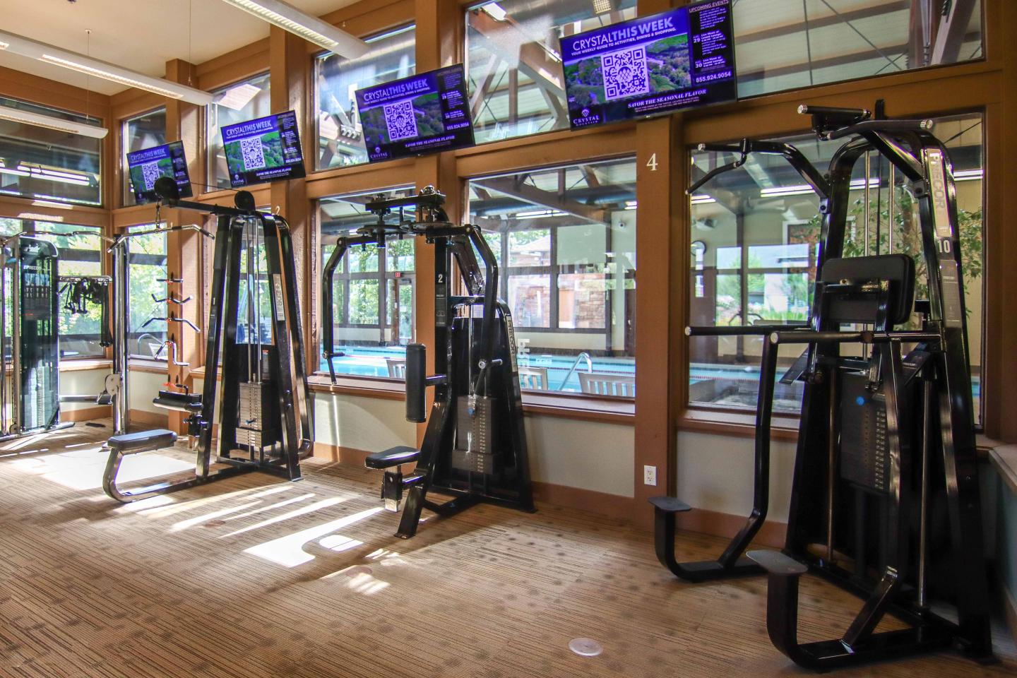 Gym interior with cable machines, treadmills, and wall-mounted TVs.