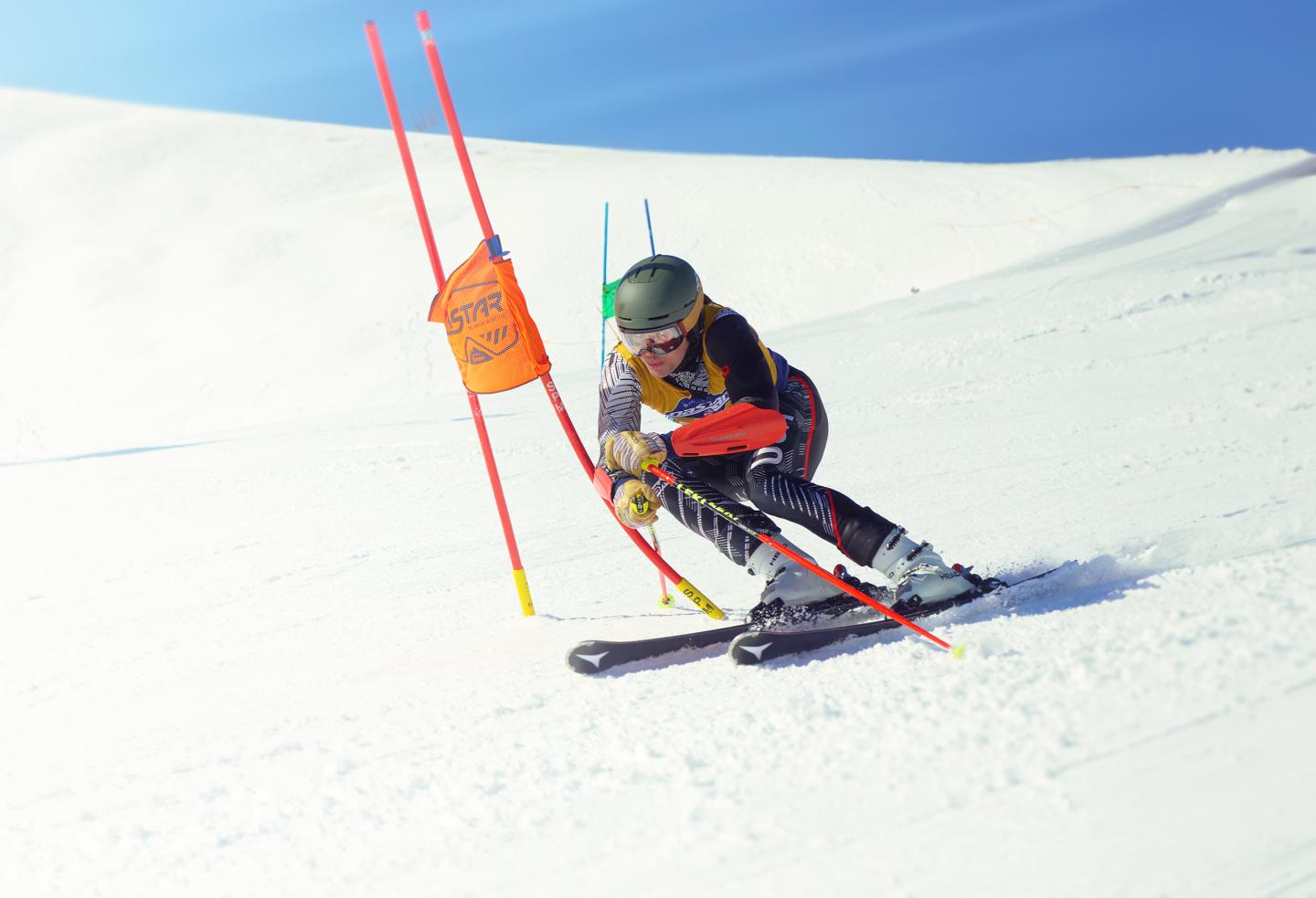 Skier racing downhill around red poles on a snowy slope.
