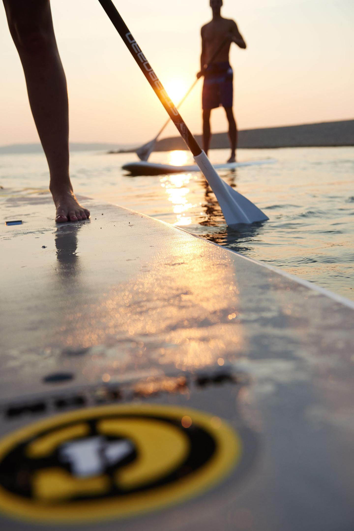 Two people paddleboarding at sunset, with sun reflecting on the water.