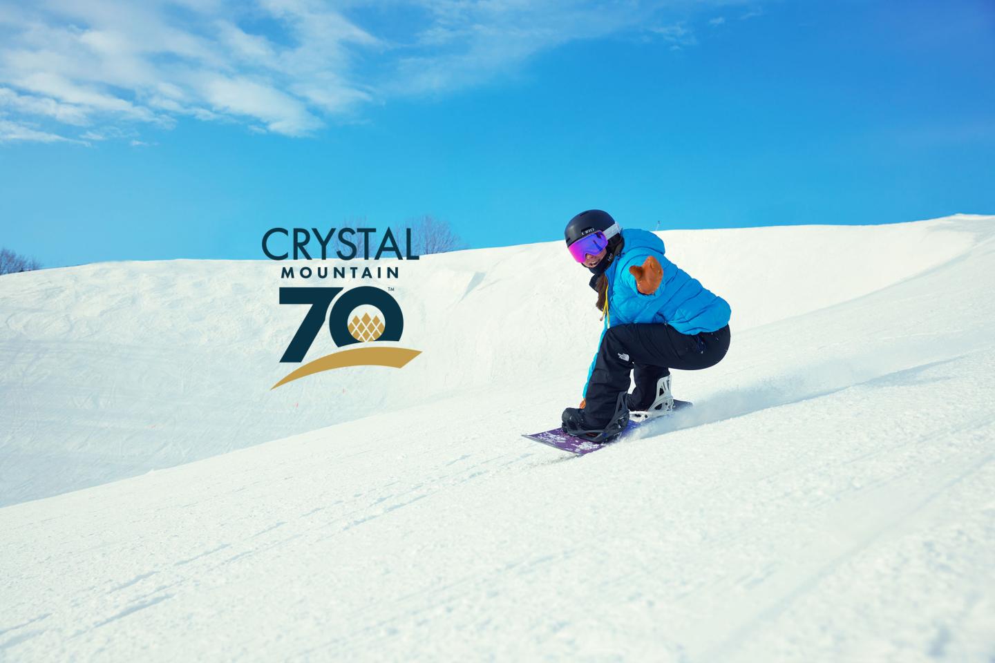 Snowboarder carving down a snowy slope beside a Crystal 70 logo.