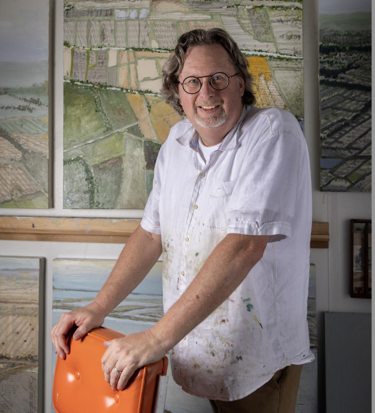 Smiling man in paint-splattered white shirt holding an orange bucket by maps.