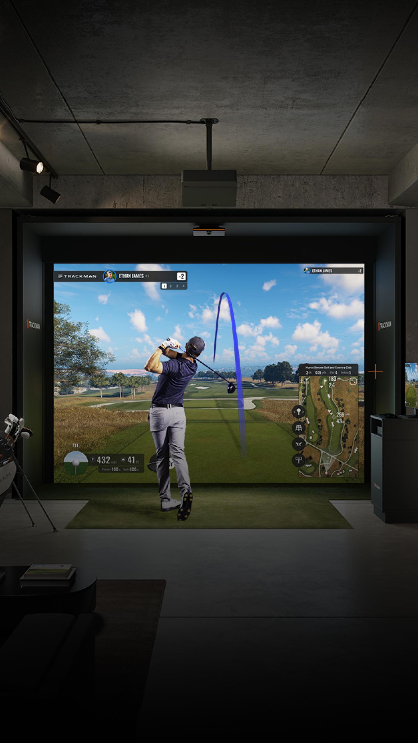 Golfer in a simulator bay swings toward a virtual course on a large screen.