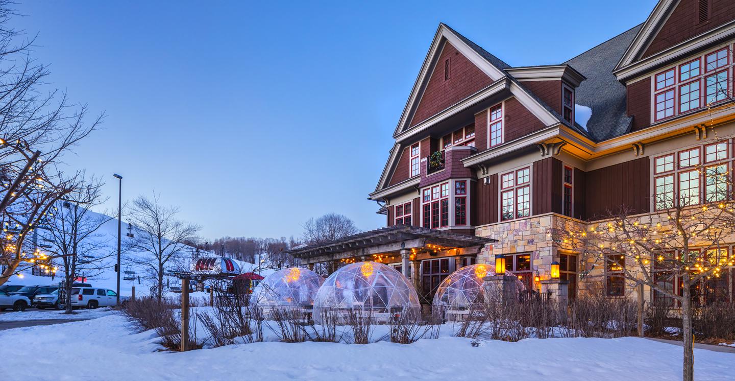Snow-covered Victorian hotel glowing warmly at dusk.